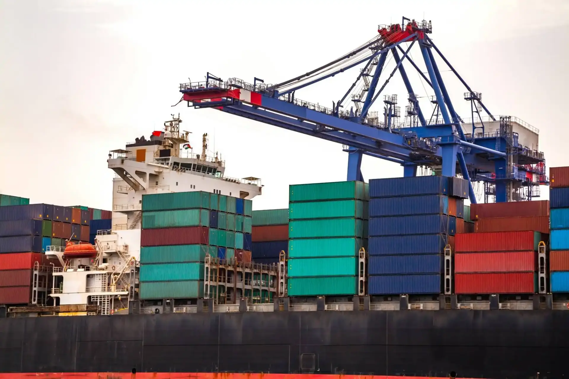 A harbor crane towers over a cargo ship with containers stacked on the deck.